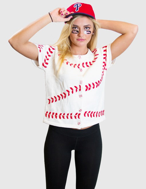 Person wearing a white short sleeve sweater with red baseball stitching design, black leggings, and a red baseball cap on a white background.