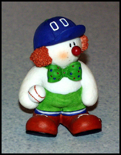 Snowman figurine with clown-like features wearing a blue cap, green bow tie, and red shoes, holding a baseball.