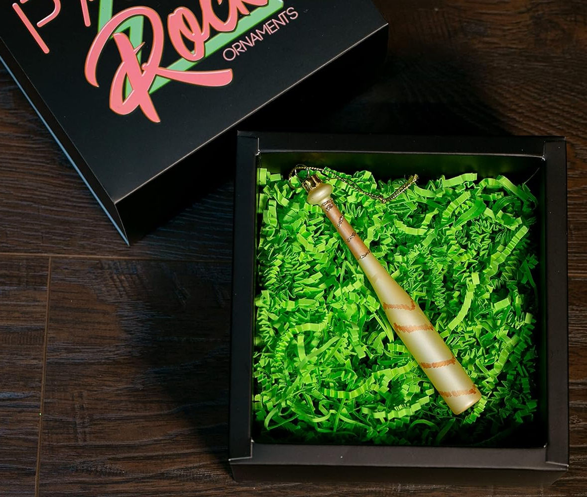 Decorative baseball bat glass ornament in a box with green shredded paper, branded 'P. Roll Ornaments'.