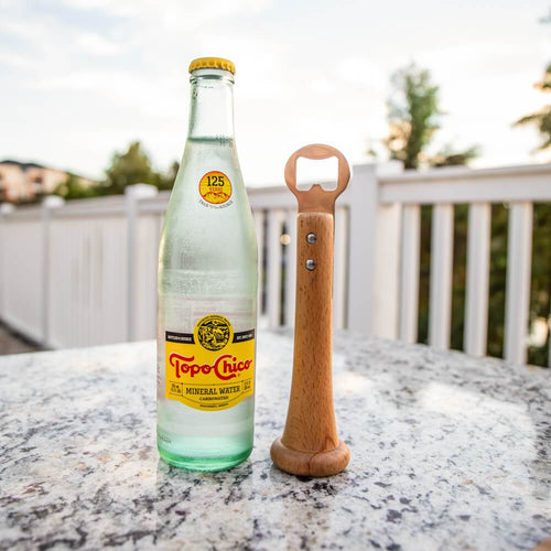 Topo Chico bottle with wooden baseball bat bottle opener on a table outdoors