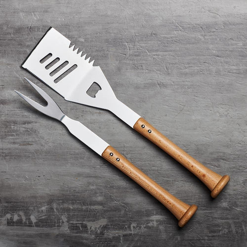 Two stainless steel barbecue utensils with wooden baseball bat handles on a gray surface