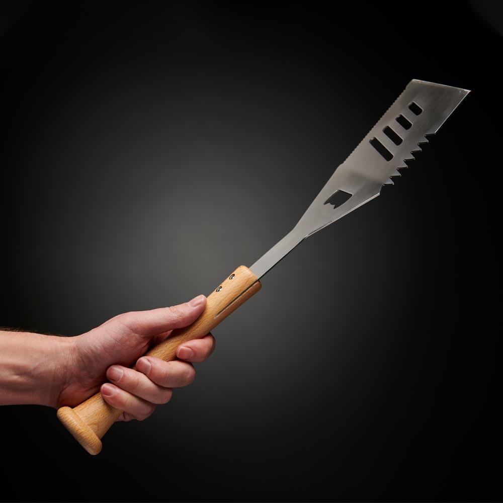 Hand holding a grill spatula with a wooden baseball bat handle against a black background