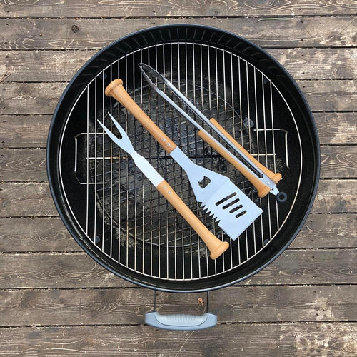Barbecue grill with baseball bat utensils on a wooden surface