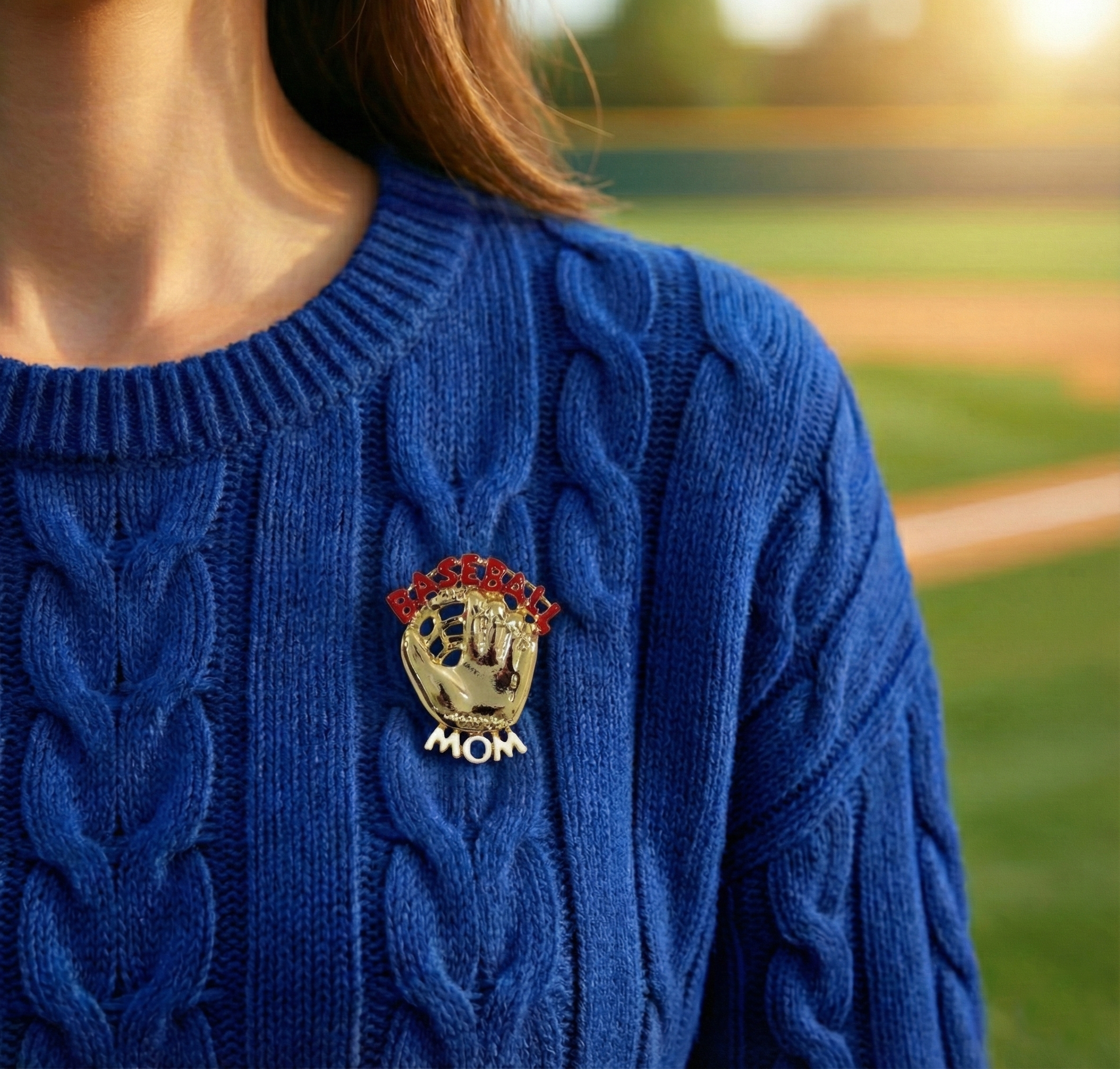 Blue sweater with a 'Mom' baseball glove brooch pin on a blurred outdoor background