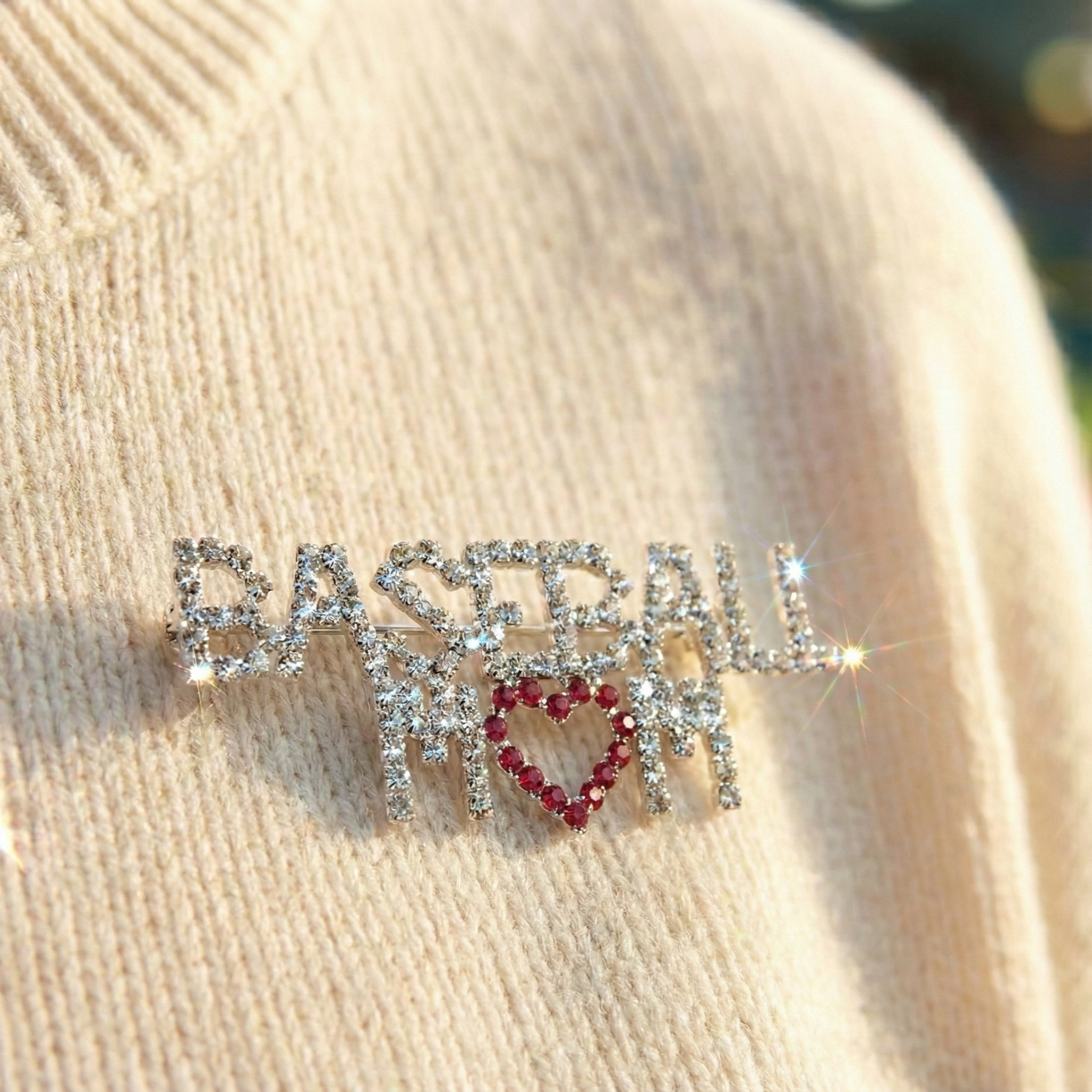 Decorative brooch with 'BASEBALL MOM' text on a beige fabric background