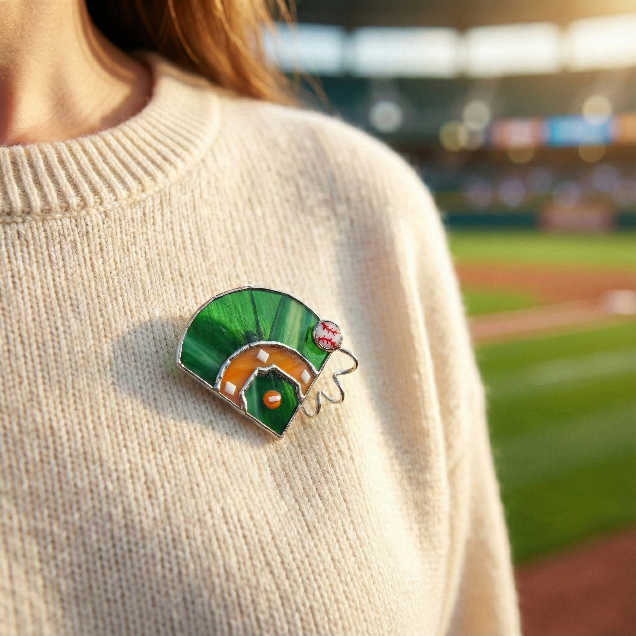 Person wearing a stained glass brooch shaped like a baseball field on a blurred sports field background