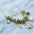 Gold necklace with heart and baseball charm on a marble background