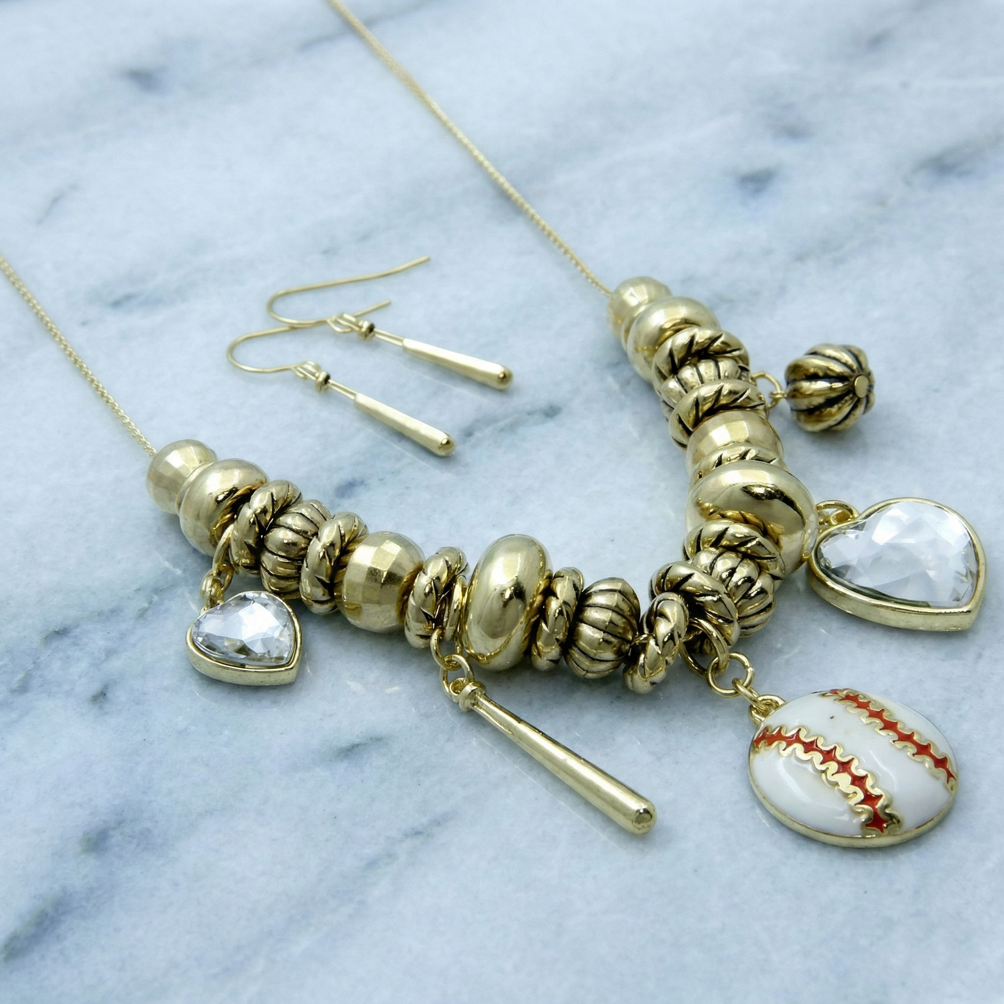 Gold necklace with heart and baseball charm on a marble background