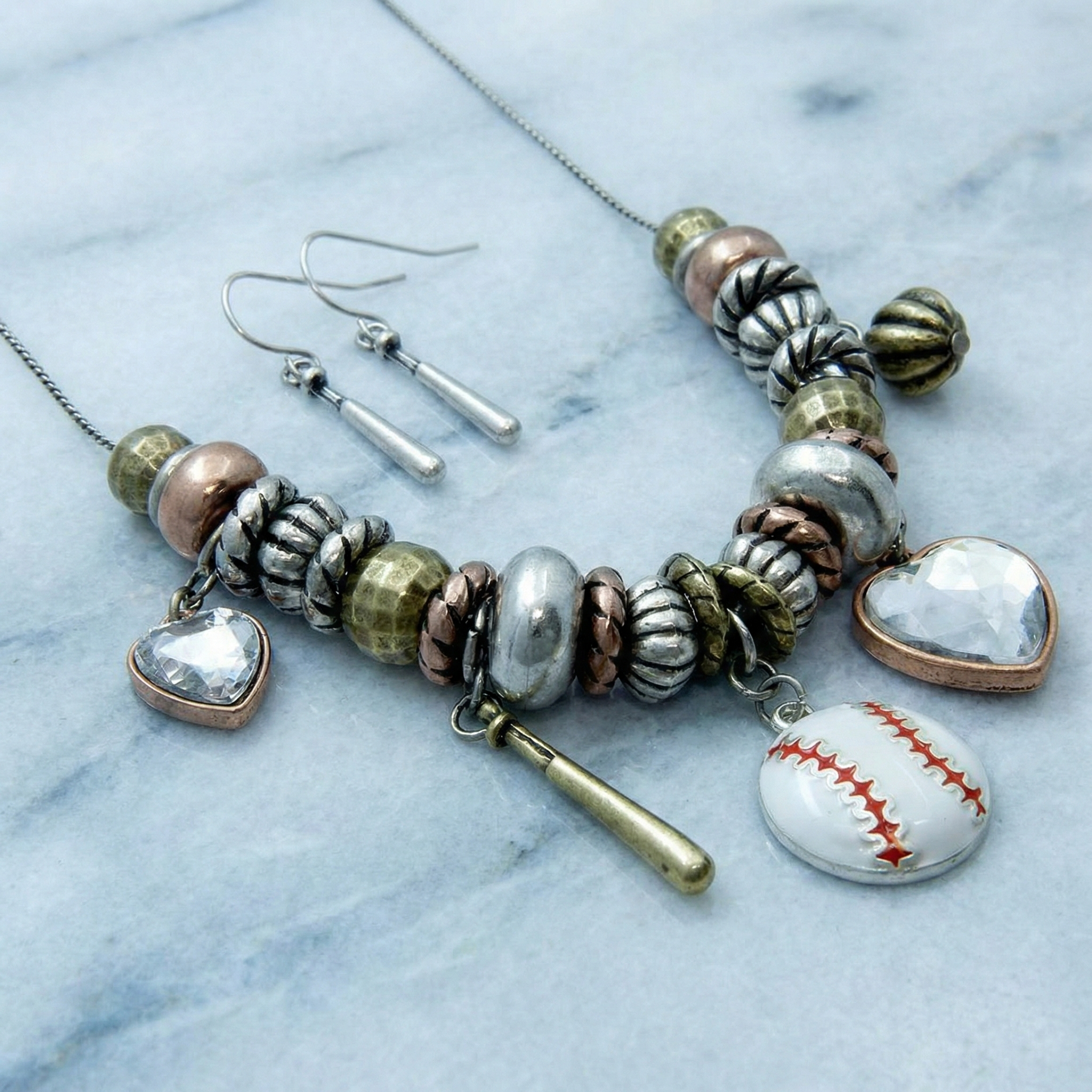 Necklace and earrings with metallic and heart-shaped beads on a marble surface