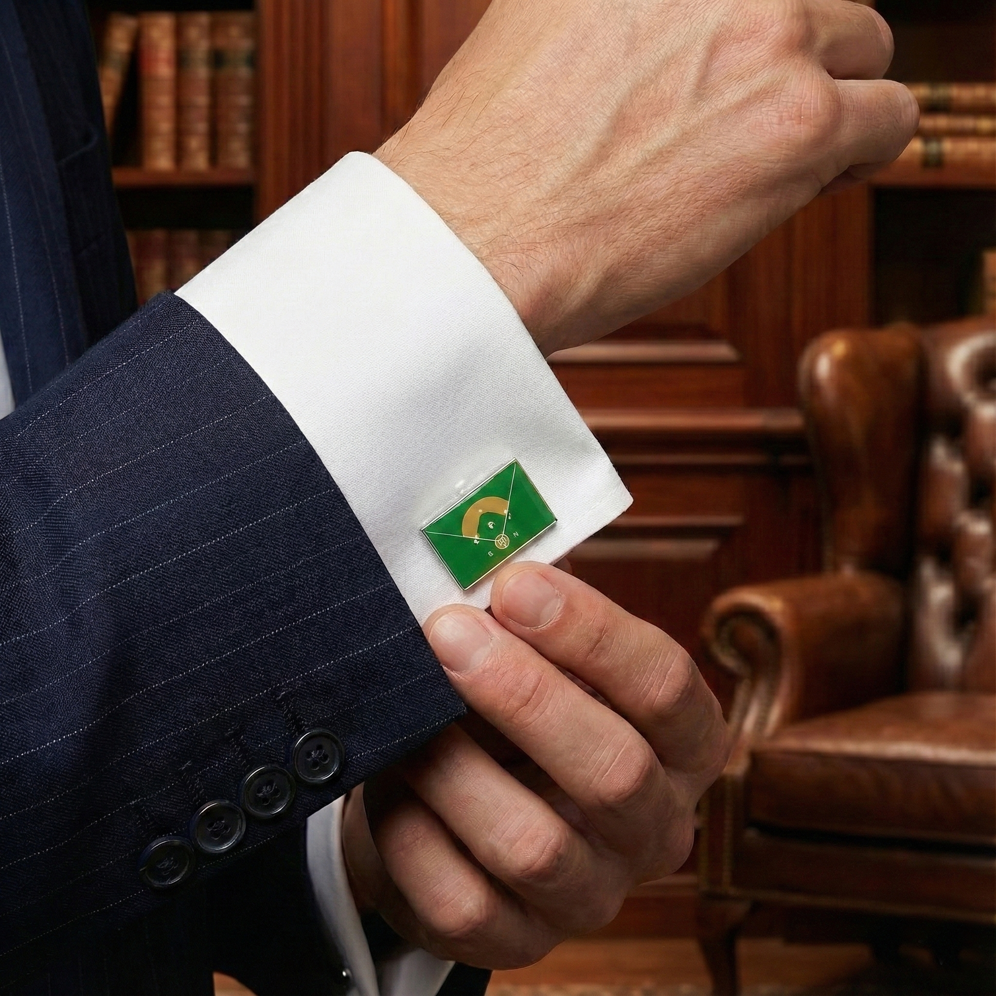 Close-up of a suit cuff with a green and white emblem, set against a background of books and a leather chair.