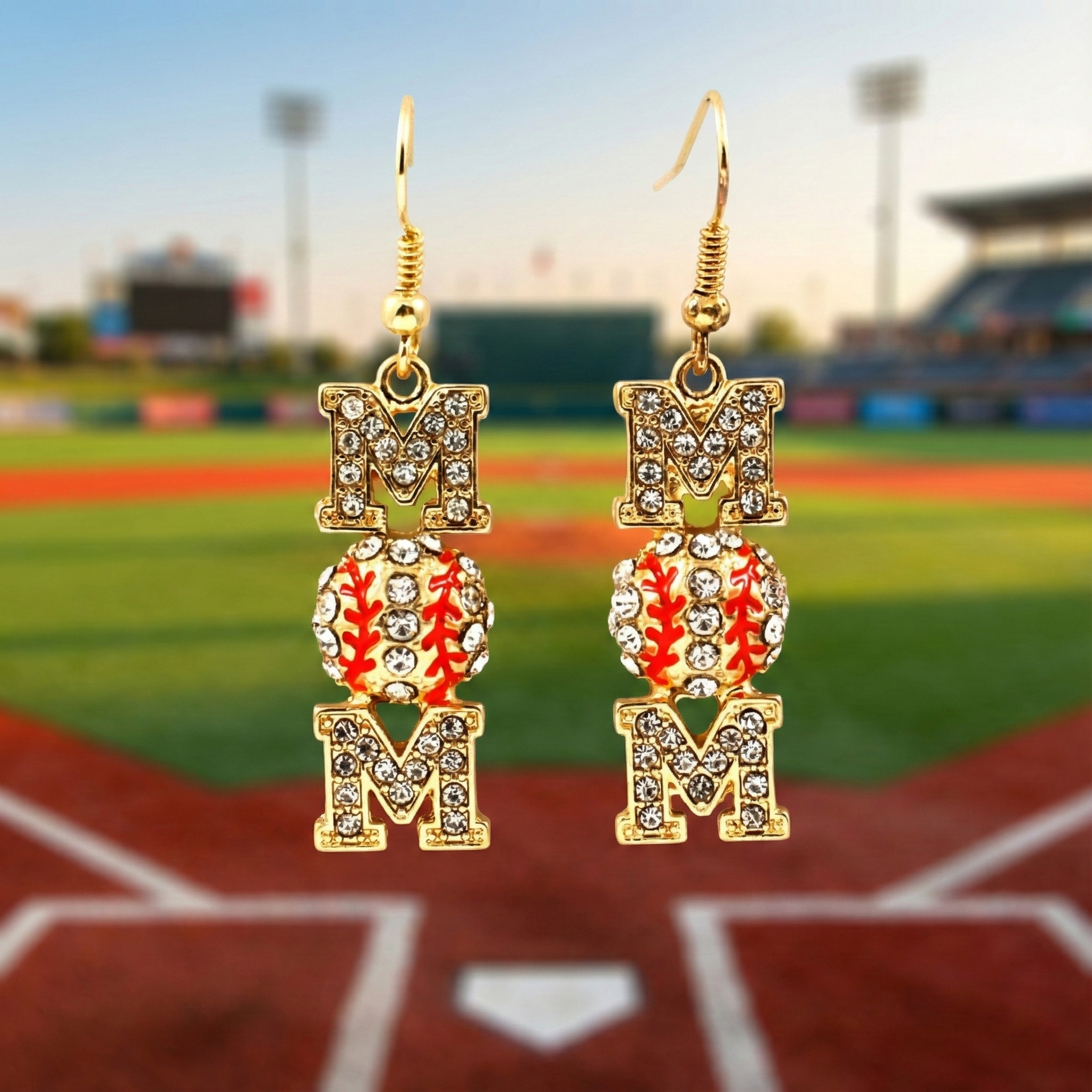 Gold 'MOM' earrings with a baseball design on a blurred baseball field background