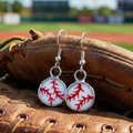 Baseball-themed earrings on a baseball glove with a blurred sports field background