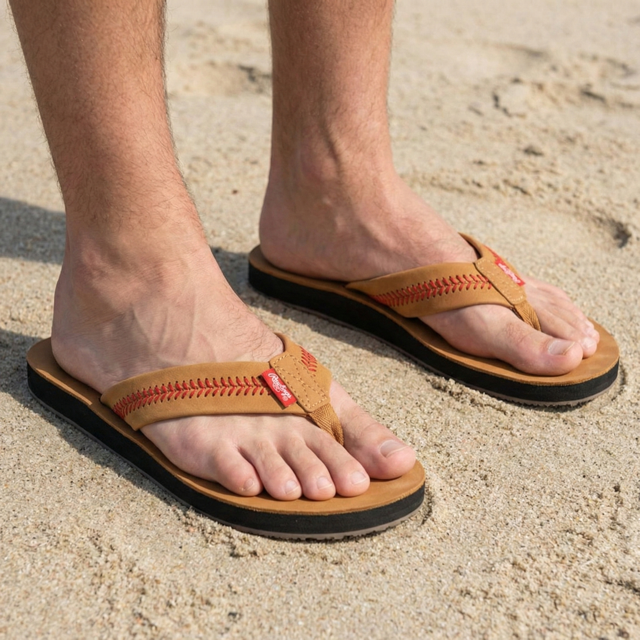 Brown baseball sandals by Rawlings worn on feet standing on sand