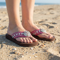 Close-up of feet wearing embellished baseball crystal sandals on a sandy beach.