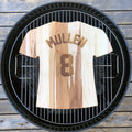 Wooden cutting board of a baseball jersey with 'Mullen' and number '8' on a grill grate.