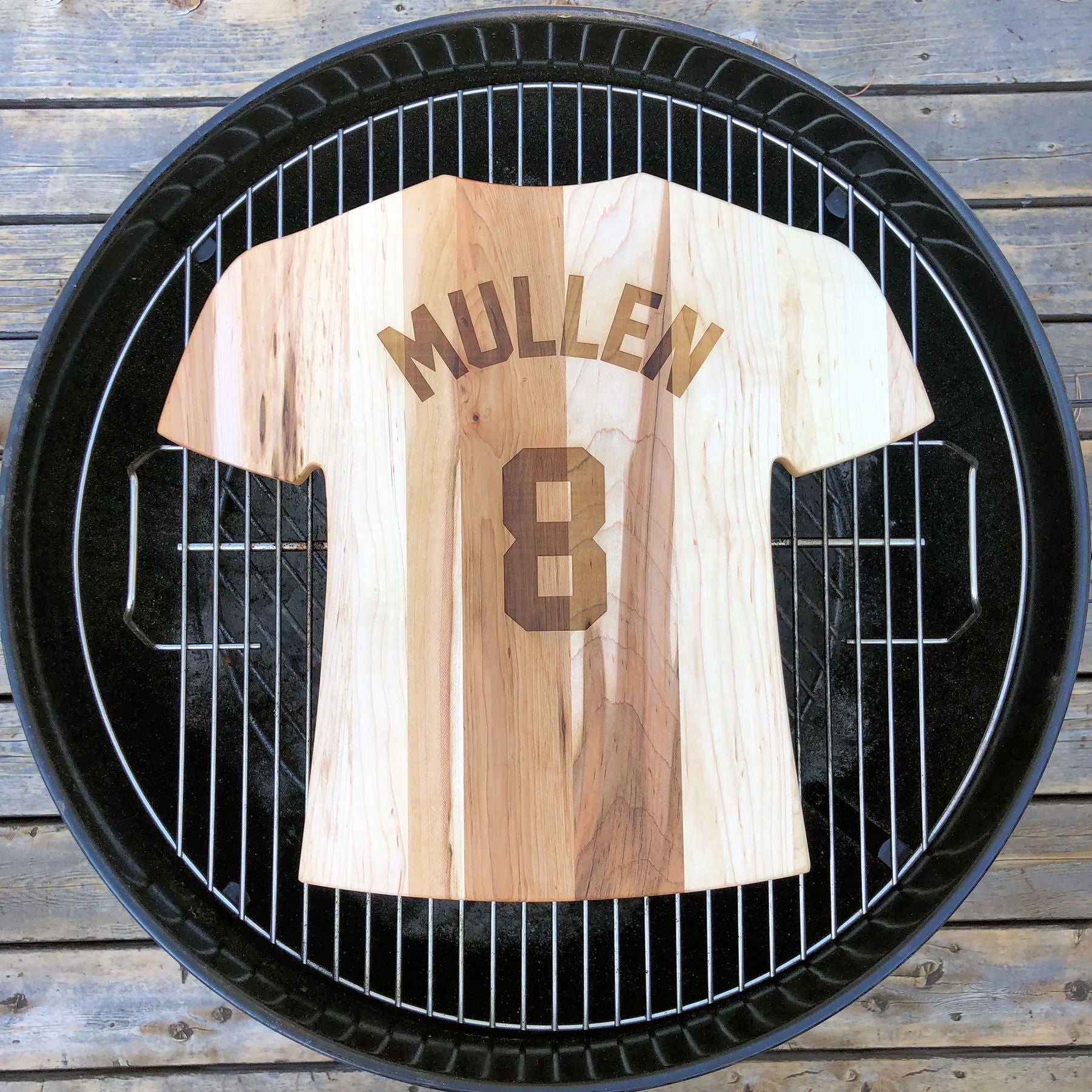 Wooden cutting board of a baseball jersey with 'Mullen' and number '8' on a grill grate.