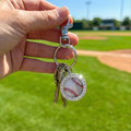 Keychain with baseball charm held by a hand on a baseball field