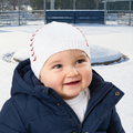 Child wearing a white knit hat with red baseball stitches and a navy coat in a snowy outdoor setting.