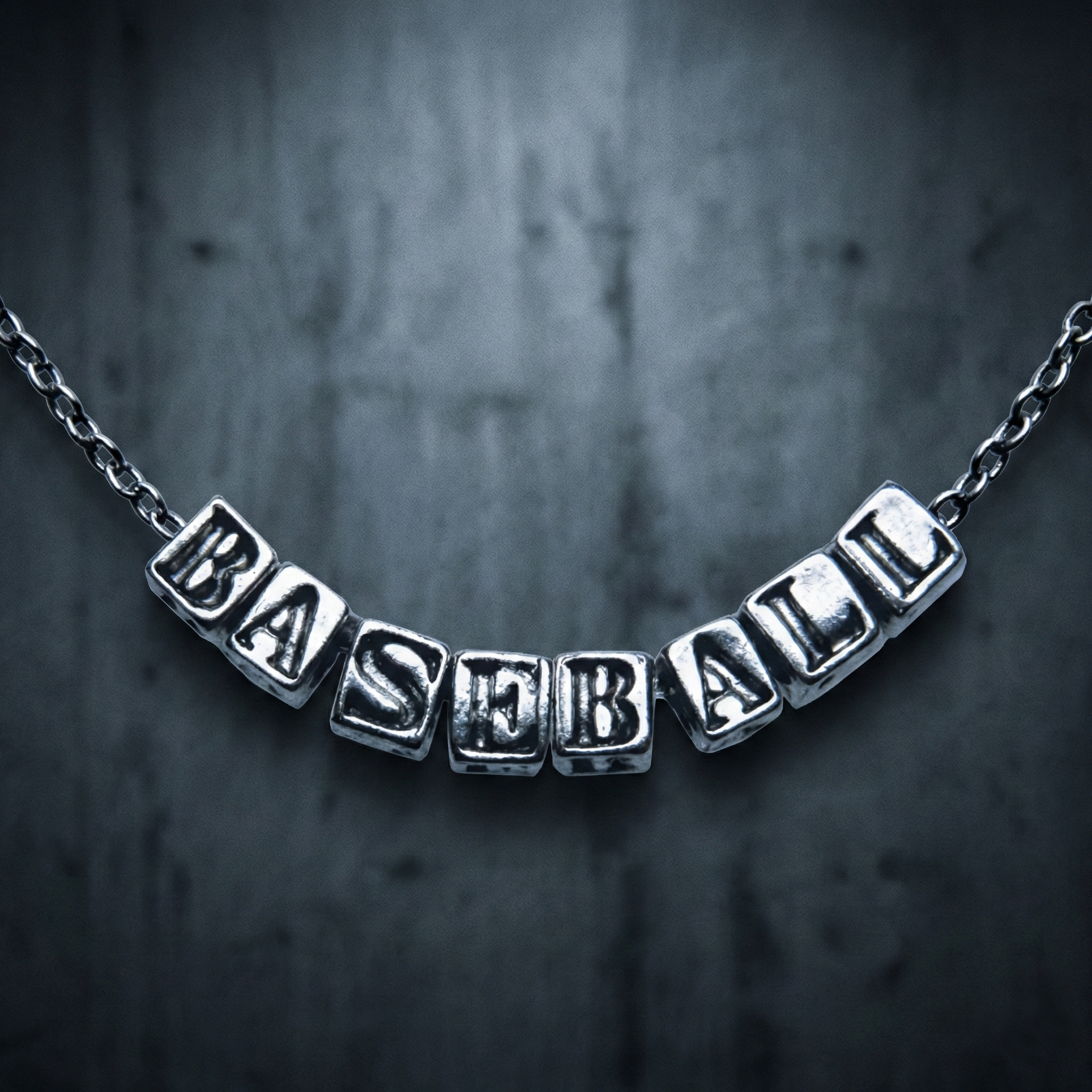 Silver Baseball Letter Necklace on blurry concrete background.
