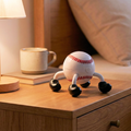 Baseball-shaped electric massager on a wooden night stand with a cup and lamp in the background