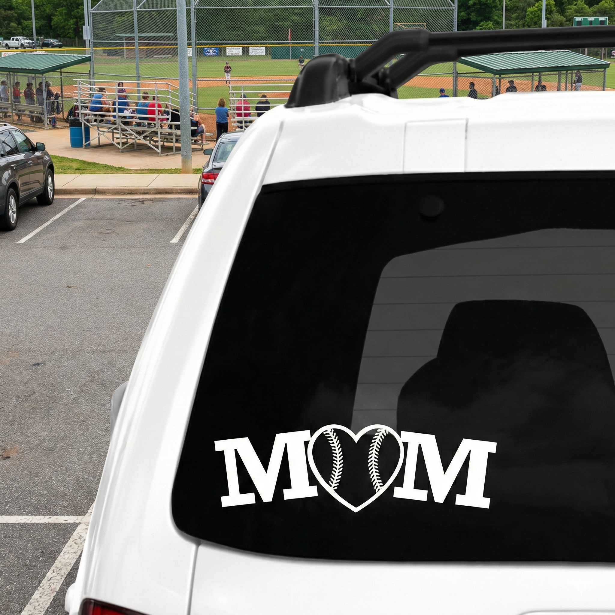 White car with Baseball Mom decal featuring a heart and baseball on a black window, baseball field background.