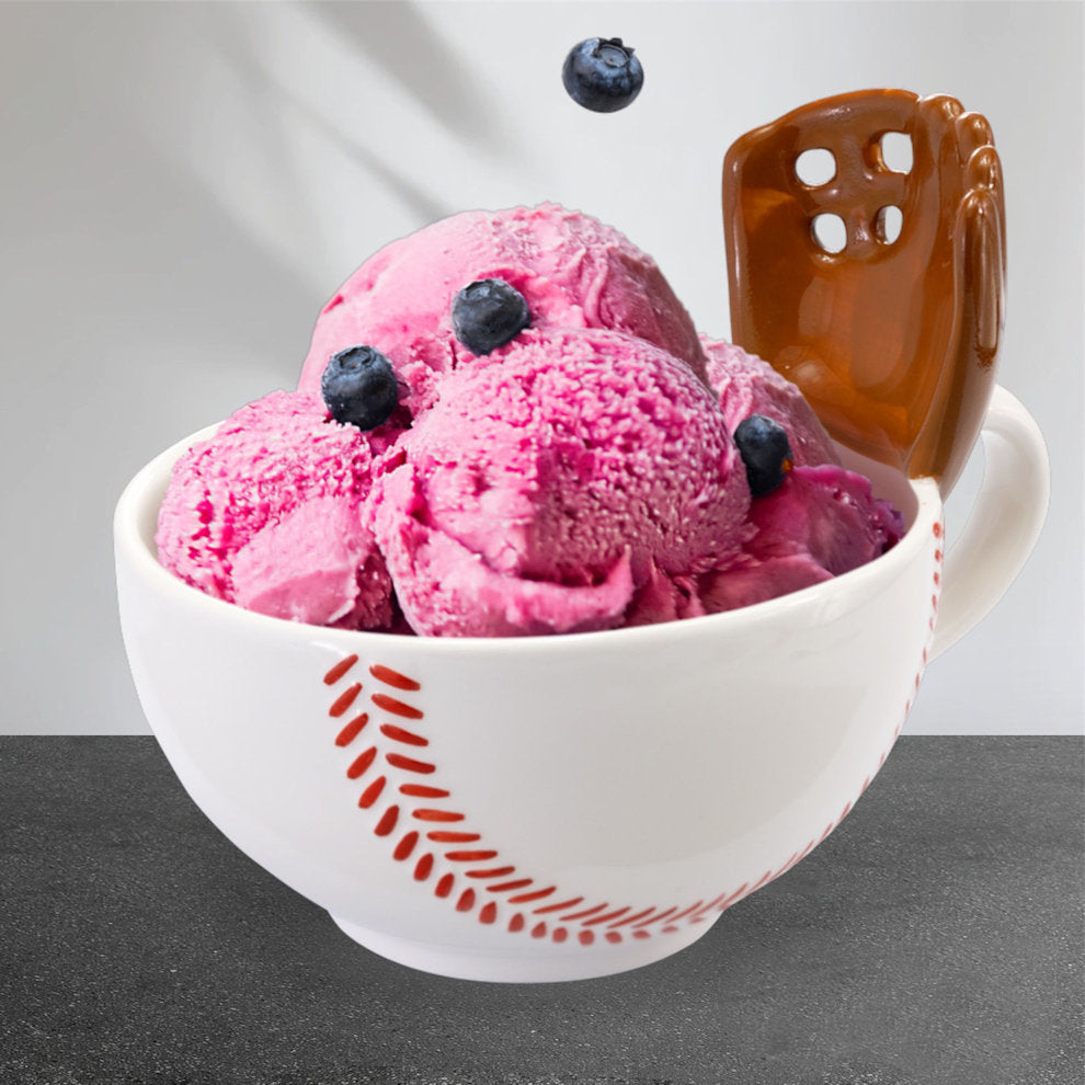 Pink ice cream with blueberries in a white baseball mug with a glove bowl with red patterns on a gray surface.