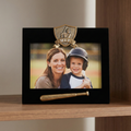 Black photo frame with MVP emblem, woman, and child holding a baseball bat on a wooden surface.