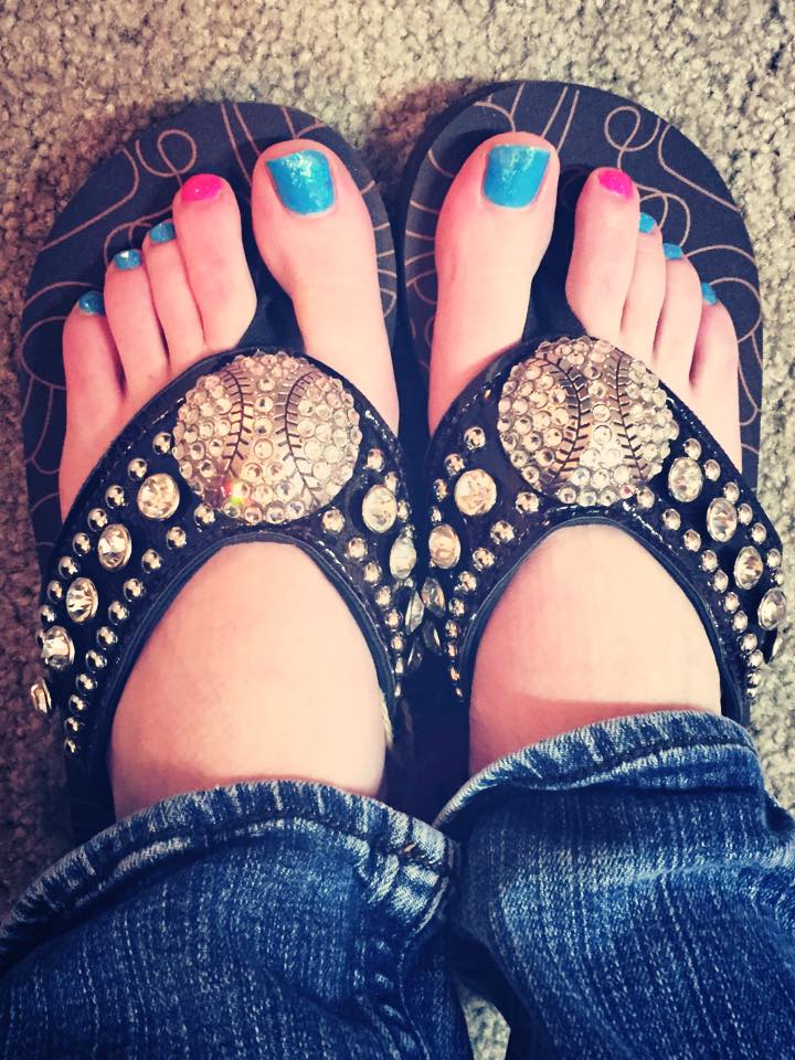 Black sandals with gold embellishments worn by a person with blue and pink nail polish.