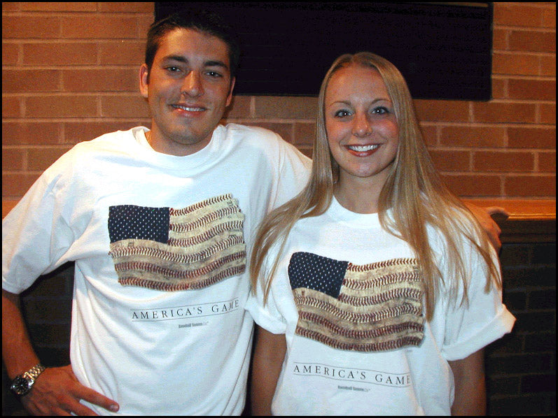 Two people wearing white t-shirts with an American flag design in front of a brick wall.