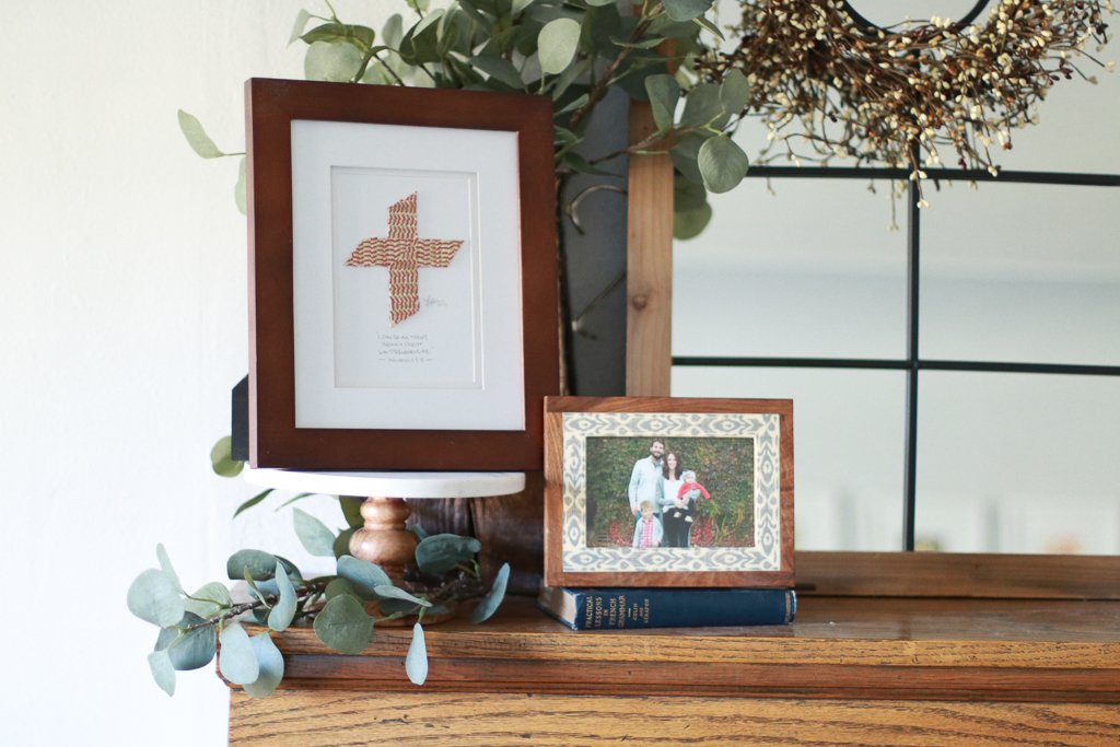 Framed baseball cross artwork and family photo on a wooden surface with greenery