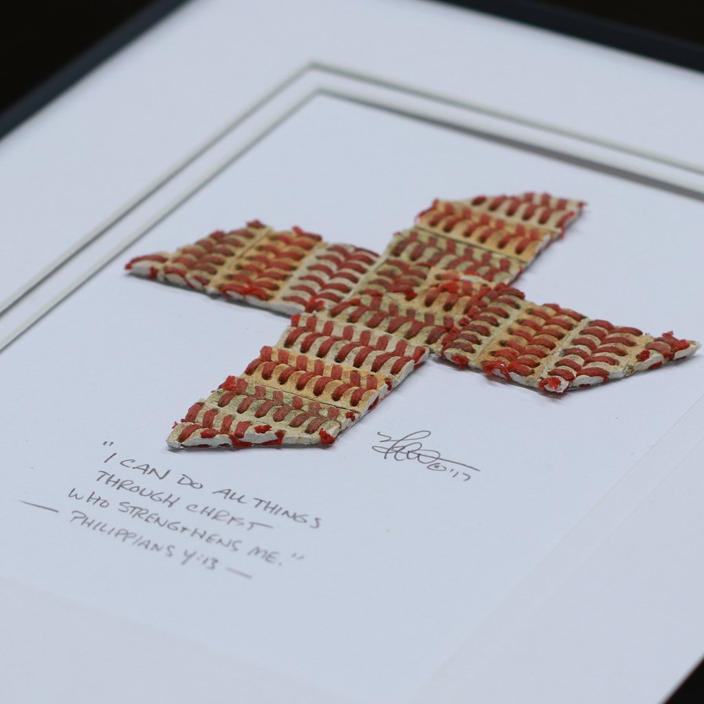 Framed cross made of red and white baseball stitches with a quote below on a white background