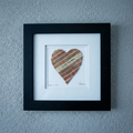 Framed heart-shaped baseball seams artwork with 'I Love You More' text on a gray wall