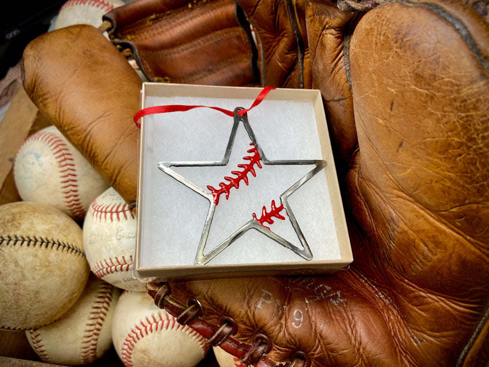 Star-shaped baseball ornament with red stitching, wrapped in paper, surrounded by vintage baseballs and a glove.