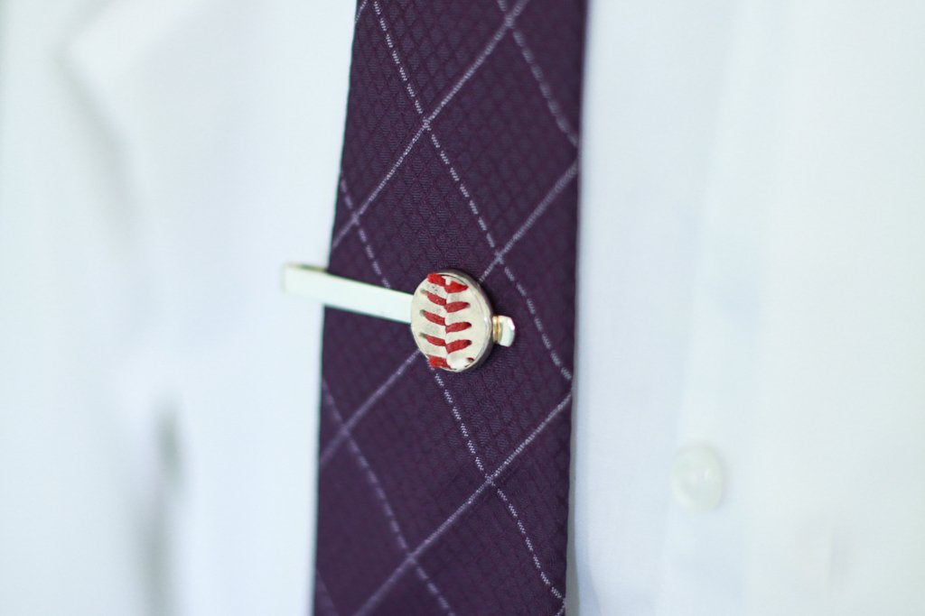 Baseball-themed tie clip on a purple checkered tie against a white shirt background