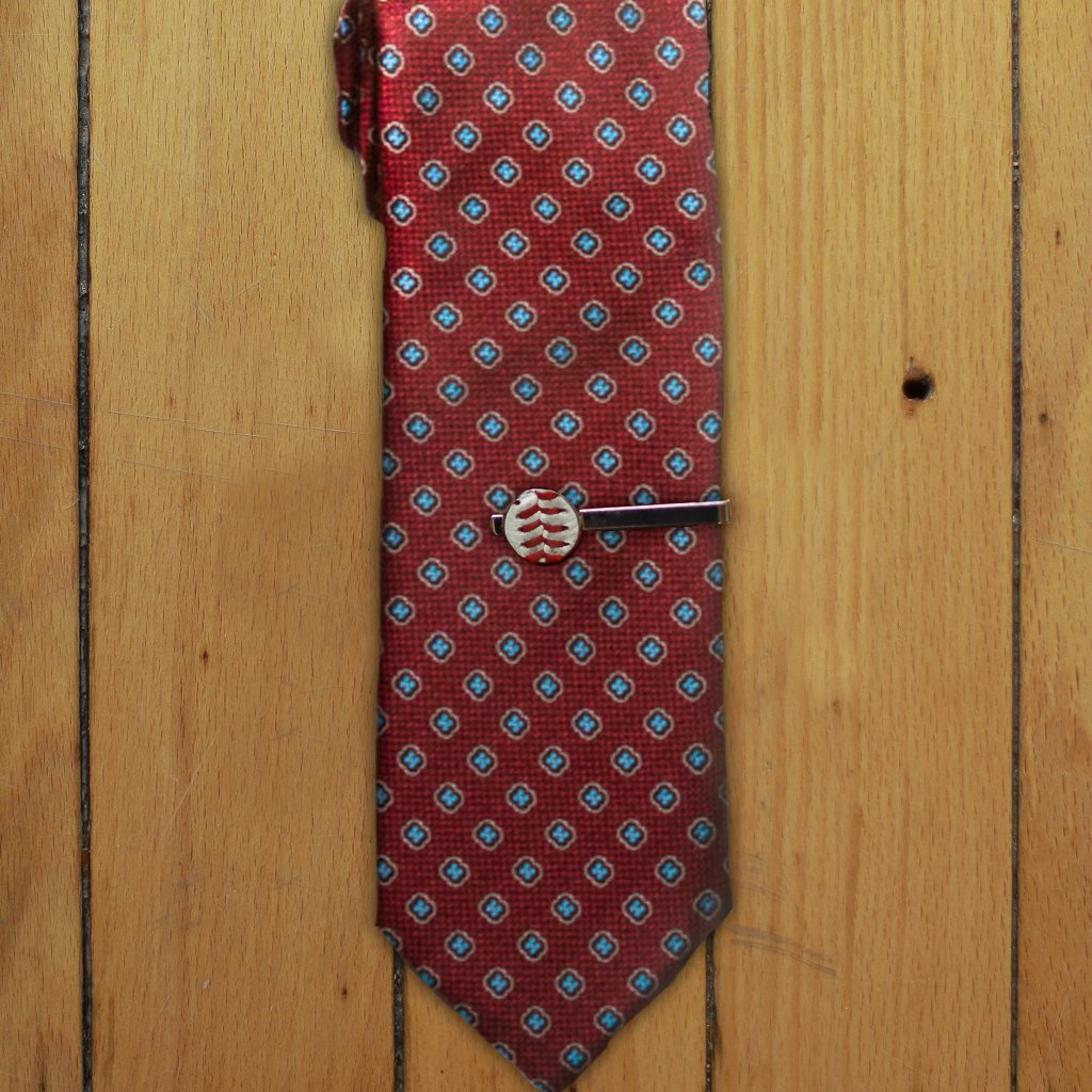 Red patterned tie with a silver baseball tie clip on a wooden surface
