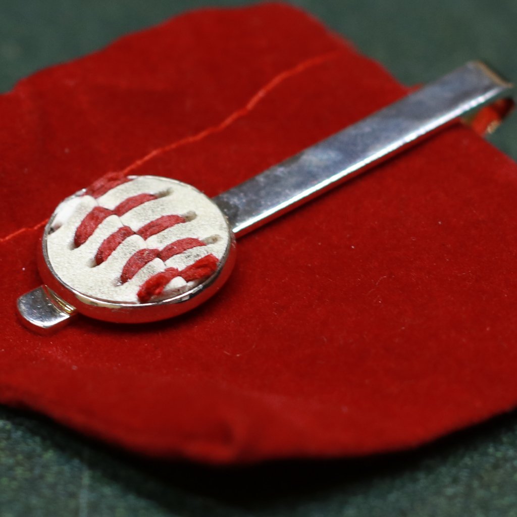 Silver baseball tie bar with red and white design on a red fabric background