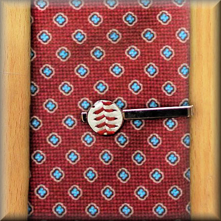 Red patterned tie with a decorative baseball tie clip on a wooden surface