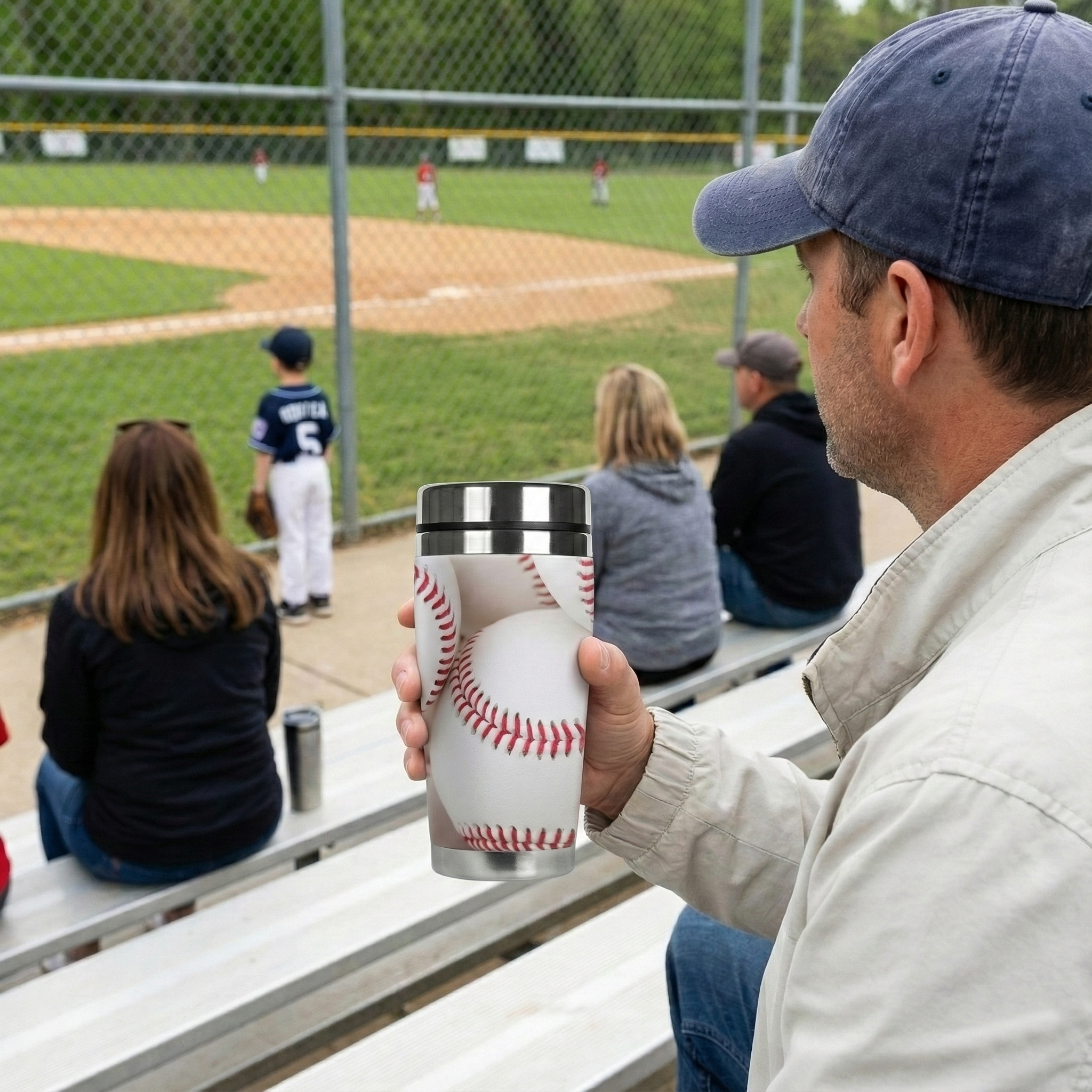 Person holding a travel mug tumbler with a baseball design at a baseball game.