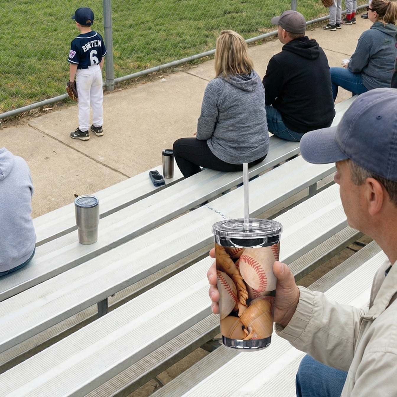 Person holding a tumbler with a baseball design at a baseball game.