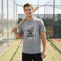 Man holding a baseball bat and wearing a gray t-shirt with a graphic design in a batting cage.