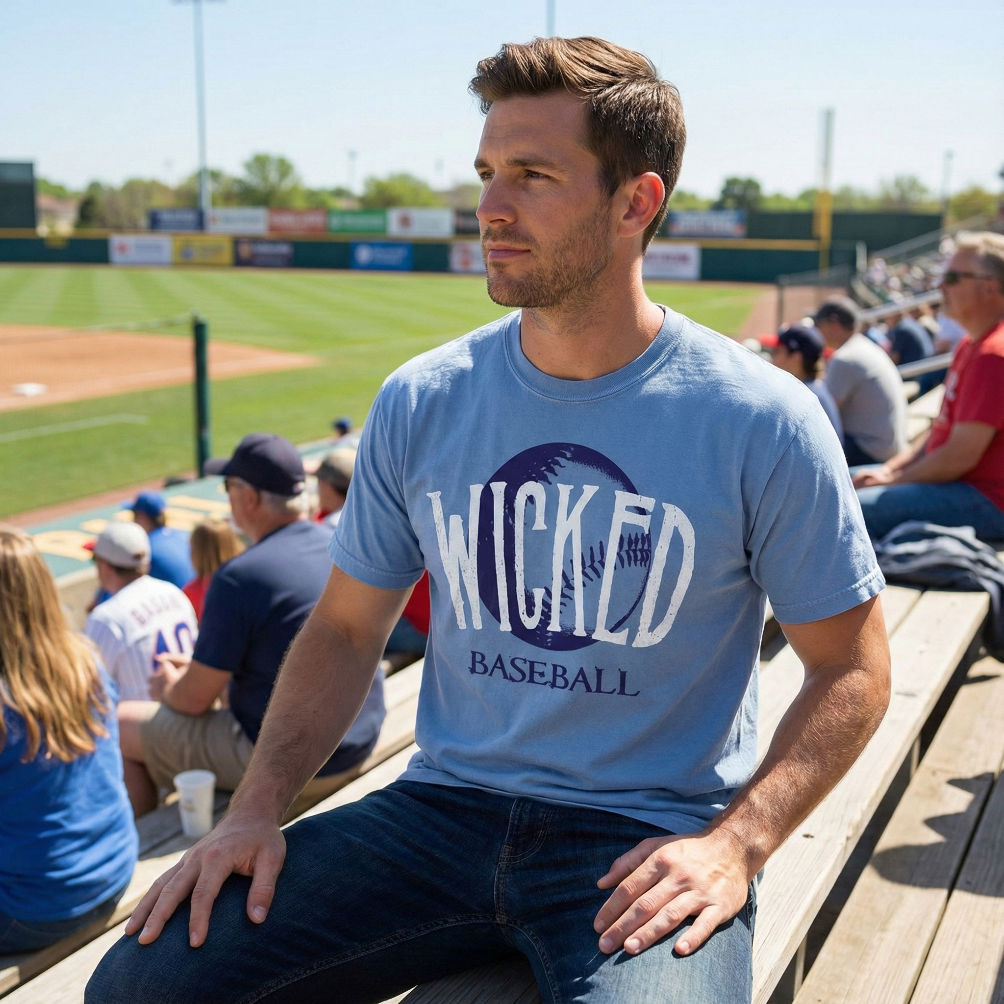 Man wearing a 'Wicked Baseball' t-shirt sitting on a bench at a baseball field.