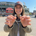 Woman holding sterling silver baseball keyring in front of Wrigley Field with a clear sky