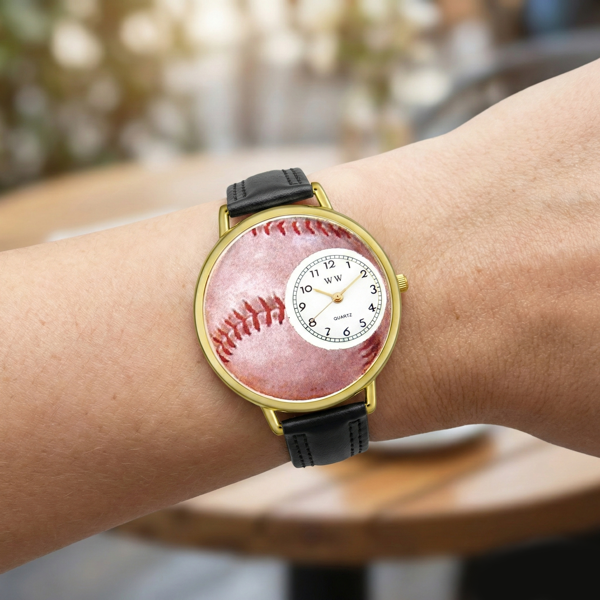 Wrist wearing a watch with a baseball design on the face, blurred background