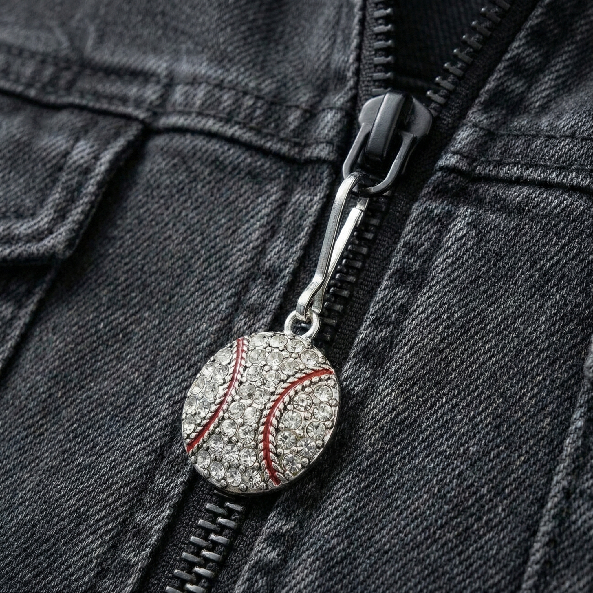 Close-up of a denim jacket with a decorative baseball charm zipper pull.