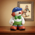 Colorful clown figurine holding a baseball on a wooden surface with a framed picture of another clown in the background.