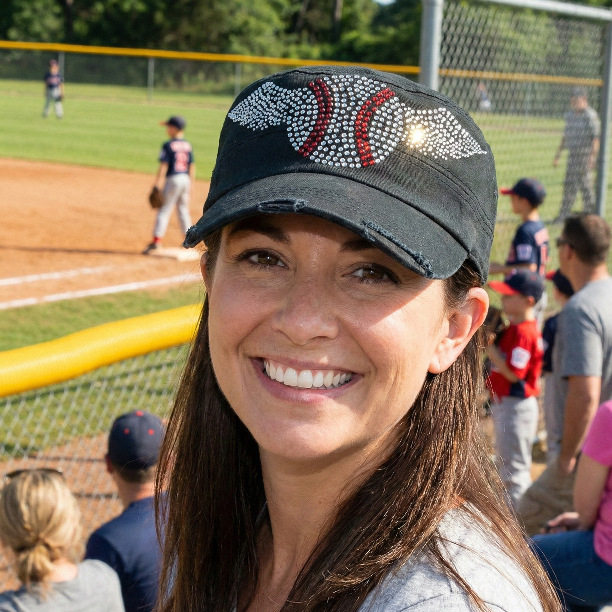 Woman wearing a baseball cap with a rhinestone design on a sports field.