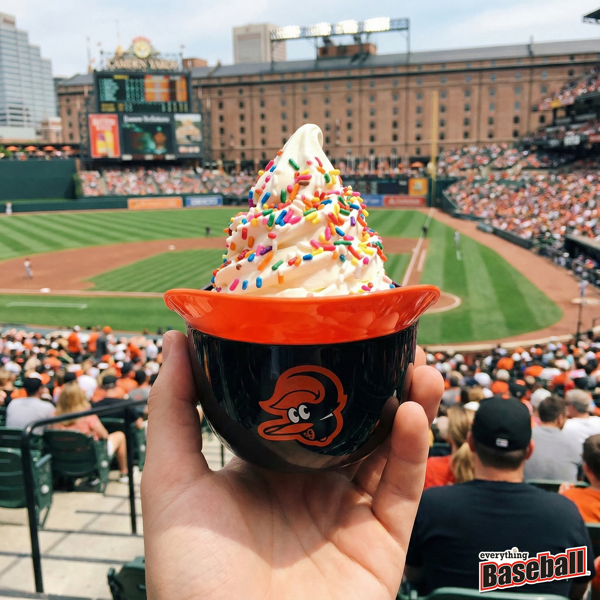 Baltimore Orioles helmet cup with vanilla ice cream and colorful sprinkles held up at a game at Camden Yards.