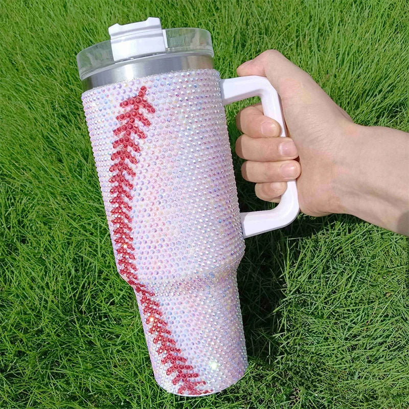 Person holding a blinged-out tumbler with a baseball design on grass