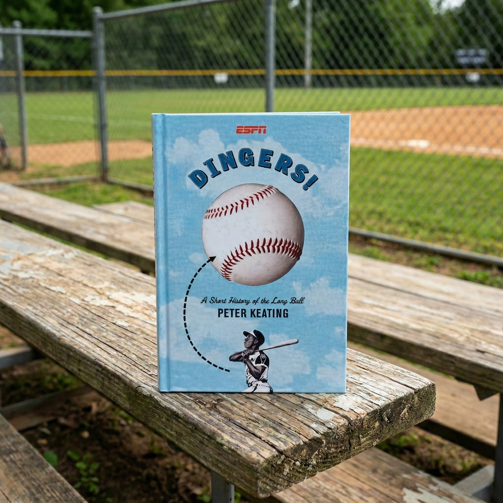 Book titled 'Dingers!' by Peter Keating on a wooden bench with a baseball field background
