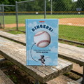 Book titled 'Dingers!' by Peter Keating on a wooden bench with a baseball field background